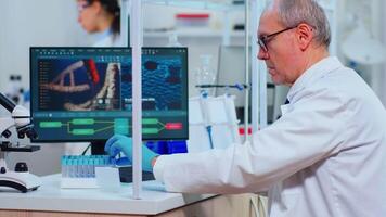 Senior man chemist examinining drug discovery using test tube in modern equipped laboratory. Multiethnic doctors examining vaccine evolution using high tech researching diagnosis against covid19 virus video