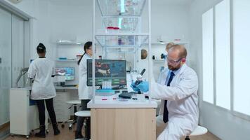 Man scientist positioning petri dish under microscope in modern equipped laboratory. Multiethnic chemist team analysing vaccine evolution using high tech for researching treatment against virus video