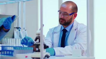 Doctor dictating to nurse virus results informations looking on test tubes in modern equipped laboratory. Doctors examining vaccine evolution using high tech researching diagnosis against covid19 video