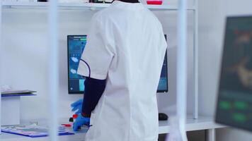 Black chemist checking blood samples taking notes on computer in modern equipped laboratory. Multiethnic doctors examining vaccine evolution using high tech researching diagnosis against covid19 virus video