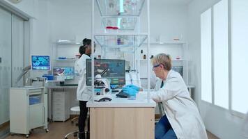 Team of elderly scientists discussing about vaccine development looking on computer in modern equipped laboratory. Multiethnic stuff analysing virus evolution using high tech for researching treatment video