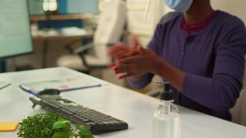 Close up of black woman using hand sanitizer while working in office room in new normal company workplace. African employee cleaning disinfecting hands using alcohol gel against corona virus. video