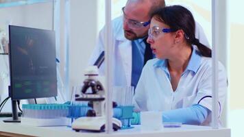Biochemist writing on computer the changes in vaccine composition in modern equipped laboratory pointing desktop. Team of doctors examining virus evolution using high tech researching diagnosis video