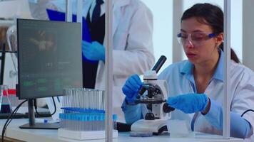 Woman chemist adjusting samples in a petri dish and examining under microscope in modern equipped laboratory. Multiethnic stuff analysing vaccine evolution using high tech for researching treatment video