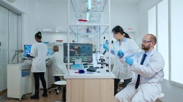 Scientist coworkers testing liquid using tube test and microscope in modern equipped laboratory. Multiethnic team analysing vaccine evolution using high tech for researching treatment against virus video