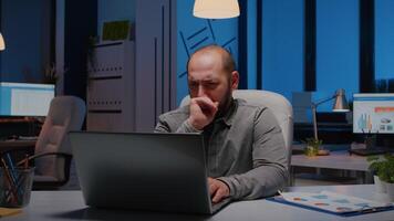 Exausta sonolento homem de negocios bocejando enquanto trabalhando às gestão projeto data limite atrasado às noite dentro comece companhia escritório. viciado em trabalho estressado empreendedor digitando financeiro estratégia em computador portátil computador video