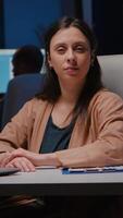 Portrait of smiling businesswoman looking into camera while sitting at desk in startup business office late at night. Manager woman planning financial statistics working at marketing statistics video
