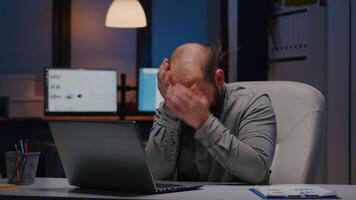 Overworked businessman rubbing face while working at financial statistics using laptop late at night in startup office. Exhausted entrepreneur analysing economic graphics before company deadline video