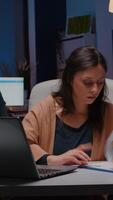 Overworked businesswoman analyzing financial graphs on clipboard comparing with economic statistics using laptop computer. Tired entrepreneur woman working in business company office late at night video