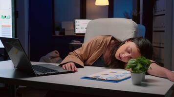 Exhausted tired businesswoman sleeping on desk table in startup business office after working at marketing strategy late at night. Workaholic tired executive manager analyzing deadline project video