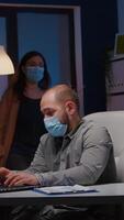 Overworked businessman with face mask against covid19 working in startup office checking management strategy late at night. Exhausted manager remains alone in company room after his collegue left video