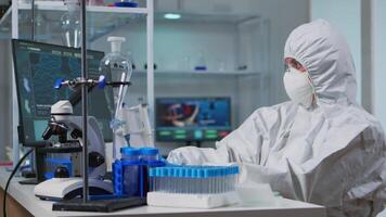 Woman scientist working at vaccine development typing on pc in coverall in modern laboratory. Team examining virus evolution in medical lab using high tech, chemistry tools for scientific research. video