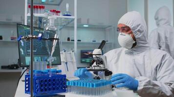 Biologist doctor in coverall checking DNA sample typing on pc in modern equipped laboratory. Team examining vaccine evolution in medical lab using high tech and chemistry tools for scientific research video