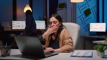 Exhausted businesswoman analyzing marketing statistics on laptop computer working in startup business company office. Tired workaholic manager remains alone in financial room after his collegue left video