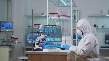 Chemist in ppe suit typing on computer checking virus development in equipped laboratory. Team doctors working with various bacteria, tissue and blood samples, pharmaceutical research for antibiotics video