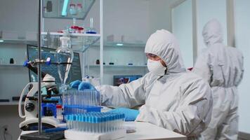 Biologist doctor in ppe suit checking liquid sample typing on pc in equipped laboratory. Team examining vaccine evolution in medical lab using high tech and chemistry tools for scientific research video
