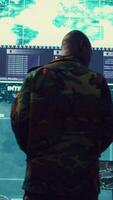 Vertical General of the army overseeing special reconnaissance mission in control center, undertake intelligence gathering operations with CCTV footage and a world map on a big screen. Camera B. video