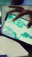 Vertical Military IT professional gathers intelligence from world map projection, tablet connected to satellite reconnaissance system to support field troops. Dispatch army command post. Close up. Camera B. video