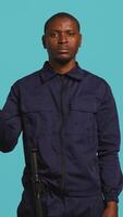 Vertical Upbeat security guard greeting people, preventing criminal activity and detaining suspects performing crimes. Portrait of jolly bodyguard waving hand towards visitors, studio background, camera B video