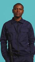 Vertical Portrait of security guard overseeing premises to prevent unwanted intrusion waving hand towards visitors. Private law enforcement worker doing greeting gesturing, studio backdrop, camera B video