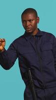 Vertical Portrait of security agent pointing finger at people, warning them while securing assigned post, studio background. African american guardian scolding trespassers, handling security breaches, camera B video
