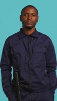 Vertical Smiling security guard saluting people during surveillance shift, ensuring protection of property and personnel, studio background. Portrait of cheerful man in uniform waving hand, camera B video