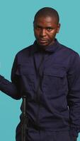 Vertical Security guard holding clock, rushing people out of property, isolated over studio backdrop. Man in uniform showing visitors time is passing, preparing for closing down location, camera B video
