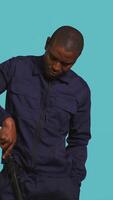 Vertical Portrait of security guard removing cane from belt while overseeing premises. Private law enforcement worker pointing to truncheon, threatening to subdue criminals, studio backdrop, camera B video