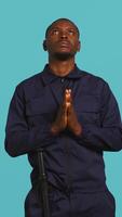 Vertical Portrait of security guard waiting for miracle, putting hands together while overseeing premises. Private law enforcement worker looking to sky, praying, studio backdrop, camera B video