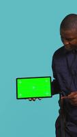 Vertical Portrait of happy security staff member showing isolated screen tablet. Joyous patrolling agent maintains secure environment, showcasing chroma key device, studio background, camera B video