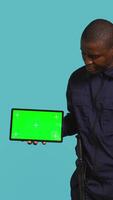 Vertical Portrait of security agent presenting chroma key tablet and securing assigned post, studio background. Guardian points finger to isolated screen device while handling security breaches, camera B video