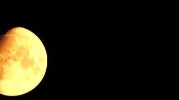 Timelapse. A glowing golden huge moon as seen from earth through the atmosphere against a starry night sky. A large moon moves across the sky, the moon moving from the left frame to the right. video