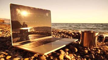 Silhouette of laptop and cup on the beach over sea sunset. Sparkling sea water on background. Freelancer, blogger working on notebook on the beach. video