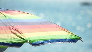 Rainbow colored beach umbrellas or parasols against blue sea during a sunny day on a beach. Symbol of vacations, relax, summer. Colorful umbrellas from the sun stand on the beach. Slow motion. video