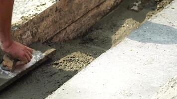 Construction, Worker Hands smooth wet cement in wooden frame at a construction site during daytime to ensure an even surface video