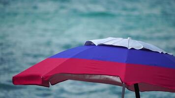 white blue red colored beach umbrellas or parasols against blue sea during a sunny day on a beach. Symbol of vacations, relax, summer. Colorful umbrellas from the sun stand on the beach. Slow motion. video