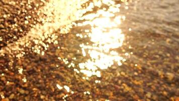 Abstract sea summer ocean sunset nature bokeh background. Small waves on azure water surface in motion blur with golden bokeh lights from sun. Holiday, vacation and recreational concept. Slow motion video
