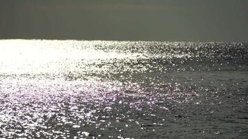 Abstract shining sun reflections on blue surface of sea waves. Bokeh sun glare reflected in water surface. The shimmering small sea waves in sun. Sea on sunny day. Natural bokeh texture. Slow motion video