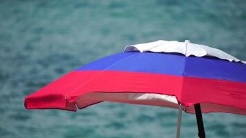 white blue red colored beach umbrellas or parasols against blue sea during a sunny day on a beach. Symbol of vacations, relax, summer. Colorful umbrellas from the sun stand on the beach. Slow motion. video