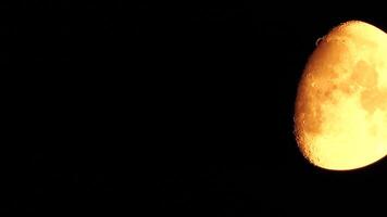 Timelapse. A glowing golden huge moon as seen from earth through the atmosphere against a starry night sky. A large moon moves across the sky, the moon moving from the left frame to the right. video