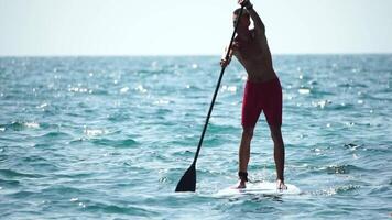 Man Sup Sea. Strong athletic man learns to paddle sup standing on board in open sea ocean on sunny day. Summer holiday vacation and travel concept. Aerial view. Slow motion video