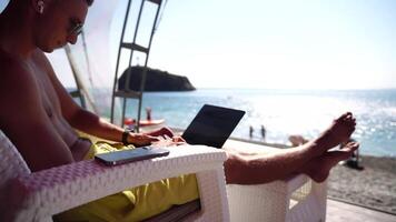 Man laptop sea. Working remotely on seashore. Happy successful man, male freelancer working on laptop on beach, relieves stress from work to restore life balance. Freelance, remote work on vacation video