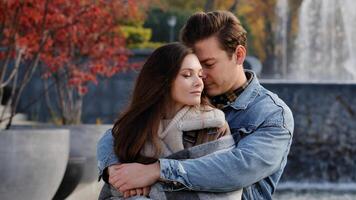 Caucasian couple lovers partners stand background of city fountain pressed closely to cheeks together spend time in autumn park on date embrace feel love emotion romantic atmosphere happy young family photo