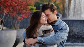 Caucasian couple lovers partners stand background of city fountain pressed closely to cheeks together spend time in autumn park on date embrace feel love emotion romantic atmosphere happy young family photo