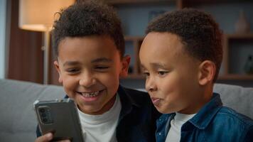 Two African American little boys brothers laughing browsing mobile phone without parents bad behavior young generation children and modern technology addicted kids siblings using funny smartphone app photo