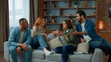 Group of diverse ethnic multiracial friends girls guys sit on sofa at home talking argue conflict friendly dispute debate discussing problem ambitious expressive men women arguing discussion indoors photo