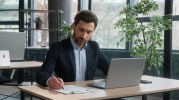 Focused adult businessman work on project in office using laptop writing notes caucasian man business leader professional employee analyze information on internet write data planning with computer app photo