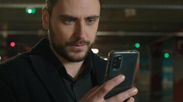 Caucasian man using mobile phone in parking night city male businessman surfing internet gadget addict texting message read good news smile order taxi driver guy client renting car with smartphone app photo