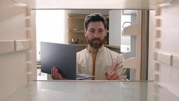 Hungry man guy open empty refrigerator confused find problem solution idea order food delivery laptop online buying products ordering goods with computer store app point of view POV from inside fridge photo