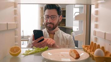 Hungry man guy open empty refrigerator poor crisis order food delivery with smartphone online buying products ordering goods with mobile phone store cellphone app point of view POV from inside fridge photo